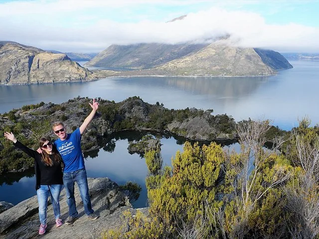 Un couple se tient sur un affleurement rocheux, bras levés devant un lac.