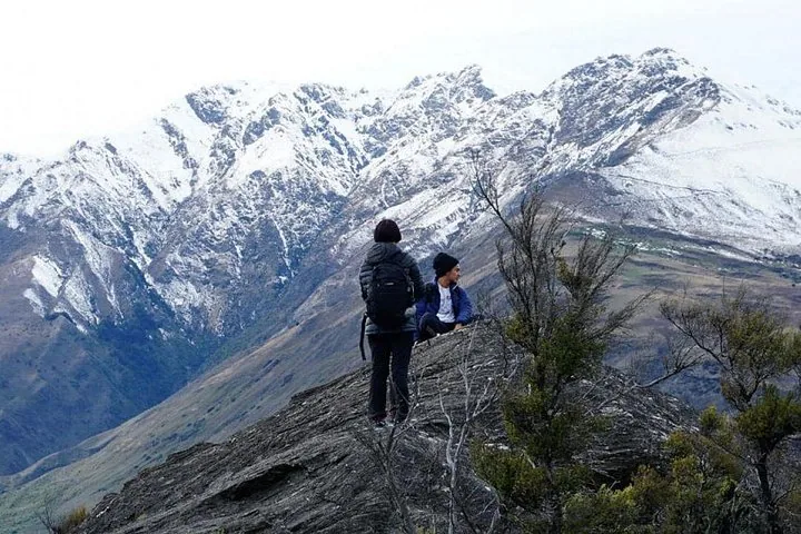 Zwei Wanderer stehen auf einem felsigen Grat, hinter ihnen schneebedeckte Berge.