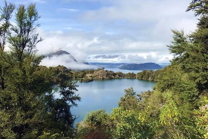 Ein ruhiger See, umgeben von üppig grünen Bäumen und Bergen in der Ferne.