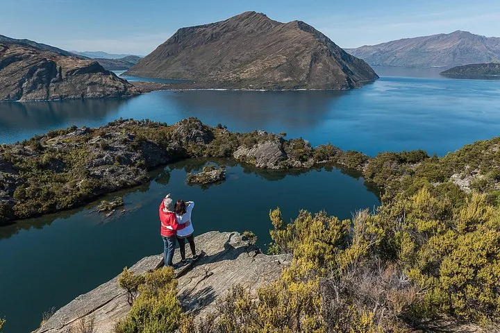 Un couple contemple un lac panoramique depuis un point de vue rocheux.